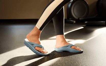 Person wearing light blue sandals on a dark floor.