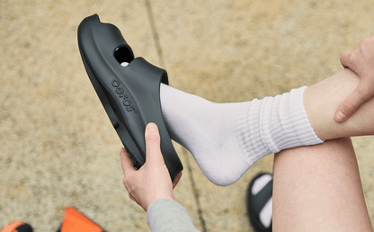 Women's OOyea Slide Sandal - Black model putting shoe on sitting down outside | lifestyle